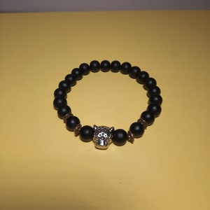May include: A black beaded bracelet with a silver jaguar head charm. The beads are matte black and the charm is detailed with a textured finish.