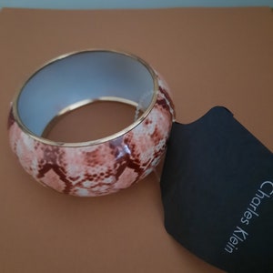 May include: A pink and brown snakeskin patterned bangle bracelet with a gold trim. The bracelet is made by Charles Klein.