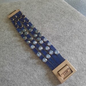 May include: A blue leather bracelet with multiple rows of light blue crystals and a silver clasp with the word "HEET" engraved on it.
