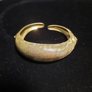 May include: A gold-toned metal bracelet with a textured, wavy design.