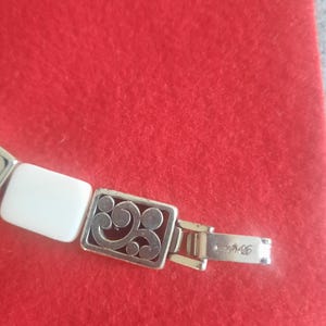 May include: Silver-toned bracelet with rectangular white and decorative silver links. The bracelet features an ornate rectangular link with a scrolling design. The clasp is marked with the brand name.