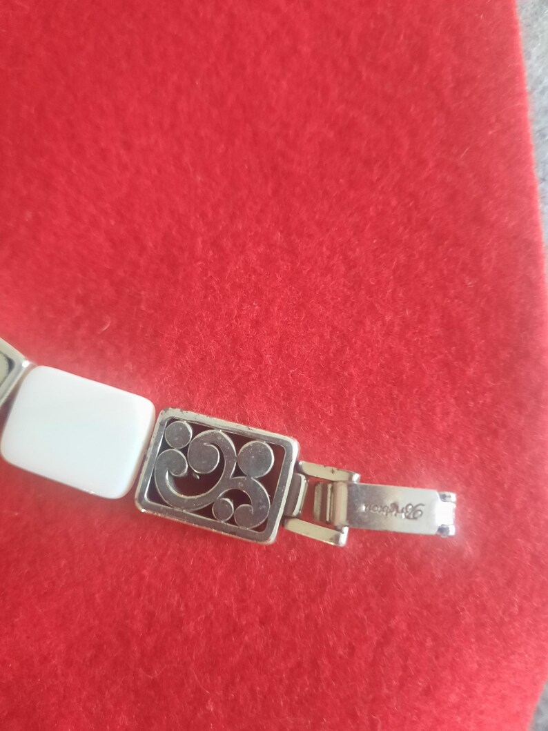 May include: Silver-toned bracelet with rectangular white and decorative silver links. The bracelet features an ornate rectangular link with a scrolling design. The clasp is marked with the brand name.