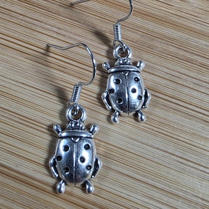 May include: A pair of silver-tone ladybird earrings. Each earring features a detailed ladybird charm with small, round spots and tiny legs. The earrings have a simple hook design for easy wear, perfect for adding a touch of nature-inspired charm.