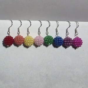 May include: A set of seven beaded ball earrings in a rainbow of colours: red, orange, yellow, pink, green, blue, and purple. Each earring has a silver-tone hook. The earrings are displayed in a row, highlighting the colour range.