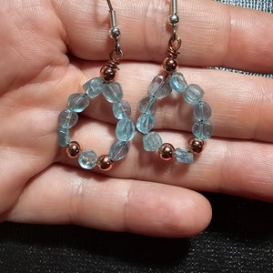 May include: A pair of silver hoop earrings with a circle of light blue gemstone beads and copper accents.