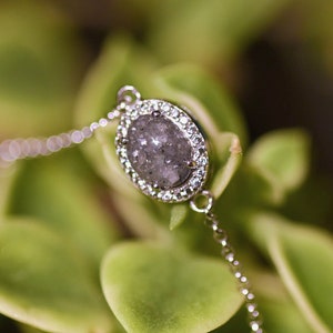 May include: A silver chain bracelet with a large oval-shaped grey gemstone surrounded by smaller clear gemstones.