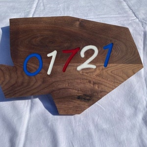 May include: A wooden sign in the shape of the United States with the numbers 01721 painted in blue, white, and red.