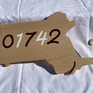 May include: A wooden cutout of the state of Massachusetts with the number 01742 painted on it in white and brown paint.