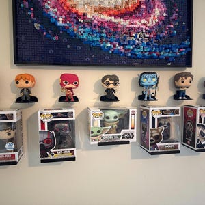 May include: A collection of Funko Pop vinyl figures displayed on small black wall-mounted shelves. The figures include characters from Harry Potter, The Flash, Avatar, and Star Wars, with several figures still inside their original cardboard boxes.