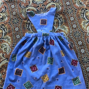 Puede incluir: Un vestido azul sin mangas con un patrón cuadrado en rojo, amarillo, verde y negro. El vestido tiene una falda fruncida y un cierre de botón en la espalda.