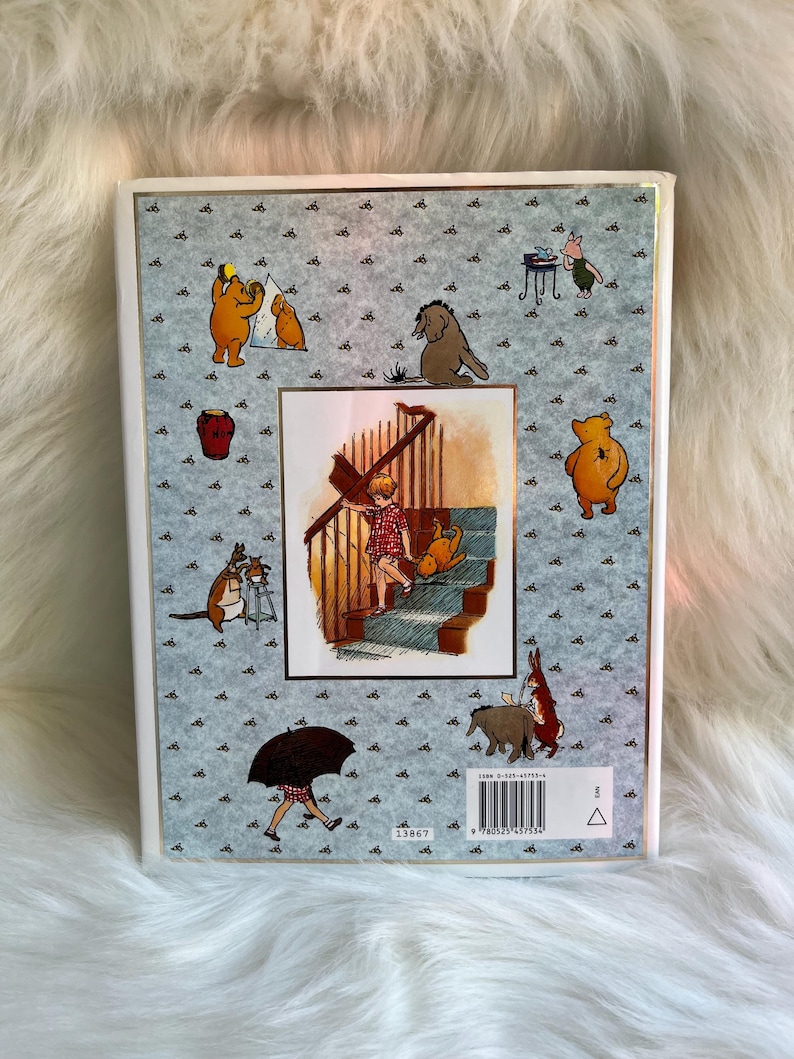 Puede incluir: Un libro de tapa dura con ilustraciones de Winnie the Pooh y sus amigos. La portada tiene un fondo azul claro con peque&ntilde;os gr&aacute;ficos de abejas negras. La imagen central muestra a un ni&ntilde;o y un perro en unas escaleras. El ISBN del libro es visible.