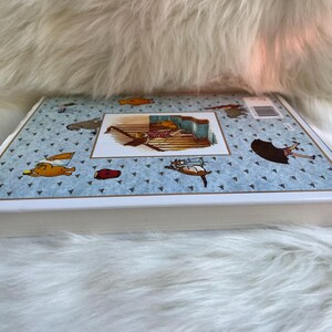 Puede incluir: Un libro infantil de tapa dura con una cubierta azul claro con peque&ntilde;os tri&aacute;ngulos azul oscuro e ilustraciones de dibujos animados de animales y objetos. El libro tiene un borde blanco y una imagen rectangular en el centro.