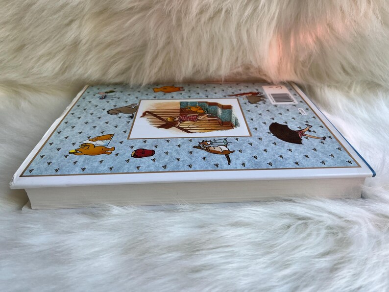 Puede incluir: Un libro infantil de tapa dura con una cubierta azul claro con peque&ntilde;os tri&aacute;ngulos azul oscuro e ilustraciones de dibujos animados de animales y objetos. El libro tiene un borde blanco y una imagen rectangular en el centro.