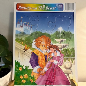 Puede incluir: Un rompecabezas de 12 piezas con los personajes de "La Bella y la Bestia". El rompecabezas muestra a Bestia y Bella en un jardín con un castillo al fondo. Para niños de 3 años en adelante.