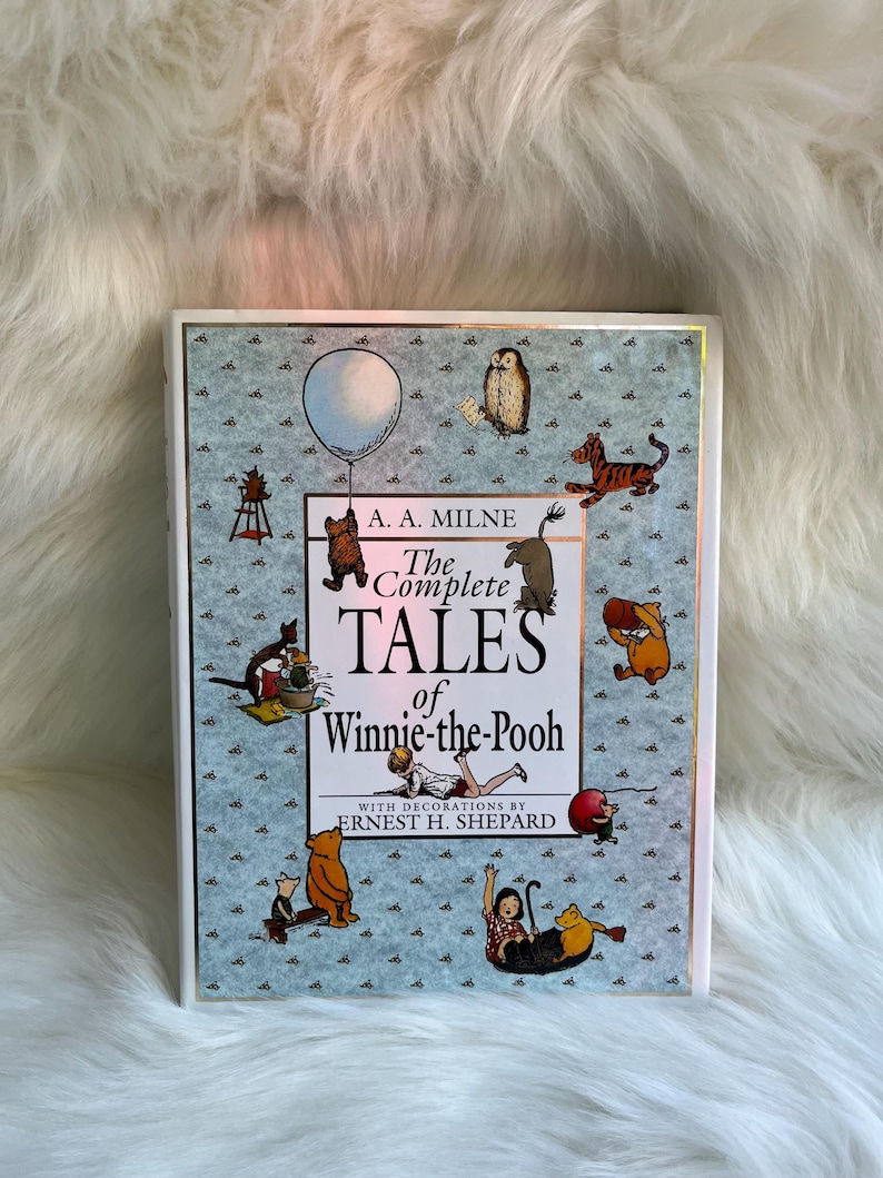 Puede incluir: Un libro de tapa dura titulado "The Complete Tales of Winnie-the-Pooh" de A. A. Milne, con ilustraciones de Ernest H. Shepard. La portada presenta ilustraciones de Winnie-the-Pooh y sus amigos, con un fondo azul claro y un borde blanco.