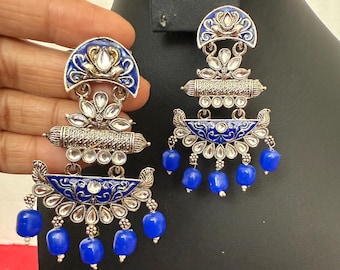 May include: A pair of silver-toned earrings with intricate blue enamel detailing and dangling blue beads. The earrings feature a floral design with clear, sparkling accents. The design is symmetrical and ornate, with a vintage aesthetic.