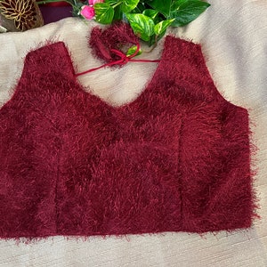 May include: A maroon fuzzy crop top with a V-neckline and a tie at the back.