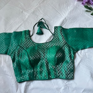 May include: A green brocade blouse with short sleeves and a round neckline. The blouse has a decorative tie at the back.