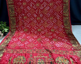 May include: A vibrant red textile with intricate patterns and gold accents. The fabric features a repeating geometric design with white and gold details. The border showcases detailed elephant and human figures, adding a cultural touch to the design.