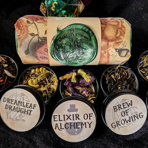 May include: An assortment of teas in small tins, each labeled with a unique name like "Song of Spring" and "Equinox Elixir." A larger package is sealed with a green wax stamp. The teas are displayed on a black surface.