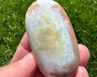 May include: A smooth, oval-shaped, white agate stone with brown and yellow markings. The stone has a natural, polished finish.
