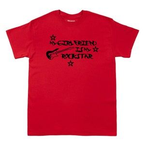 May include: Red t-shirt with a black graphic that says "My Girlfriend Is My Rockstar" with a guitar and stars.