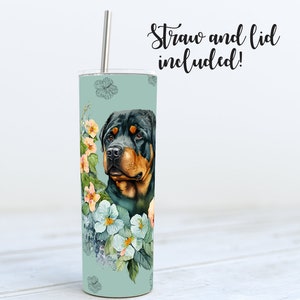 May include: A stainless steel tumbler with a floral design and a Rottweiler dog's head. The tumbler is teal blue with white and pink flowers. The text "Straw and lid included!" is at the top of the image.