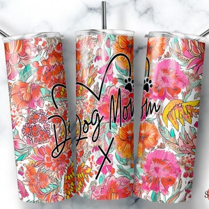 May include: Three stainless steel tumblers with a white background and a colorful floral pattern. The center tumbler has the text "Dog Mom" in black cursive writing with a heart and paw print.