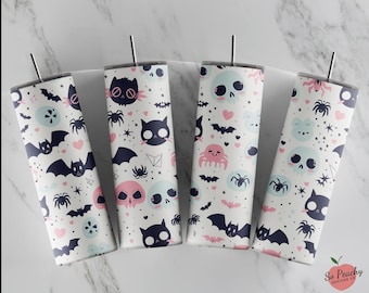 May include: Four white Halloween-themed tumblers with stainless steel straws. Each tumbler features a repeating pattern of bats, spiders, skulls, cats, and hearts in pink, blue, and black. The tumblers are designed for cold beverages.