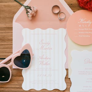 May include: A wedding invitation suite with a pink and white color scheme. The invitation features the names "Emily Martin and Andrew Walker" and the date "08.14.25". Heart-shaped sunglasses and wedding rings are also present.