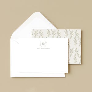 Può includere: Set di cancelleria bianco con una busta aperta, una carta con monogramma e una carta fantasia. Il monogramma presenta le lettere "N" e "L" all'interno di uno stemma. La carta fantasia ha un motivo floreale verde chiaro.