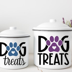 May include: Two white enamel canisters with black lids and black lettering. The smaller canister says "DOG treats" with a blue paw print and a heart. The larger canister says "DOG treats" with a purple paw print and a heart.