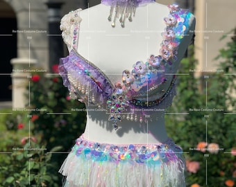 May include: A white, iridescent, sequined and feathered costume top and skirt set. The top features a purple and white bra with a matching choker necklace. The skirt is a white, feathered mini skirt with iridescent sequins.