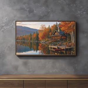 May include: A rectangular framed wall art print depicting a wooden cabin beside a calm lake during autumn. The scene features vibrant orange and yellow trees, a wooden dock with two chairs, a red canoe, and mountains under a soft morning sky.