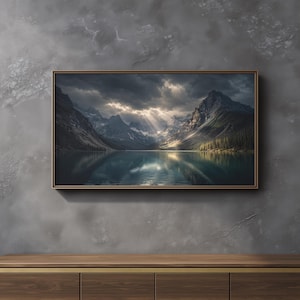 May include: A rectangular framed wall art print featuring a landscape of a calm lake surrounded by dark, jagged mountains under a dramatic, cloudy sky with sunbeams breaking through the clouds to illuminate the water and the mountain peaks.