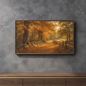 May include: A rectangular framed wall art print depicting a sunlit autumn forest path covered in fallen orange and yellow leaves. A stone wall lines the left side of the path, while a wooden fence runs along the right side under golden trees.