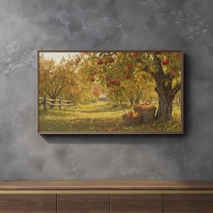 Puede incluir: Una impresión de arte mural rectangular enmarcada que representa un huerto de manzanos en otoño. El paisaje muestra hileras de árboles cargados de manzanas rojas, dos cestas de madera llenas de fruta cosechada y un edificio al fondo.