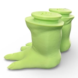 May include: Two light green, foot-shaped bottle stoppers. Each stopper has a flat, circular top and a curved, boot-like base with toes. The stoppers are made of a smooth material and are set against a white background.