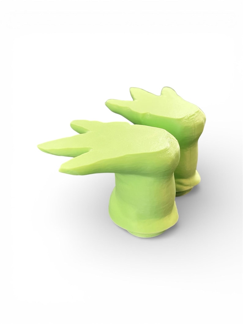 May include: Two light green, abstract, hand-shaped decorative objects. Each has a rounded base and three finger-like extensions. The objects are set against a white background, with soft shadows suggesting a three-dimensional form.