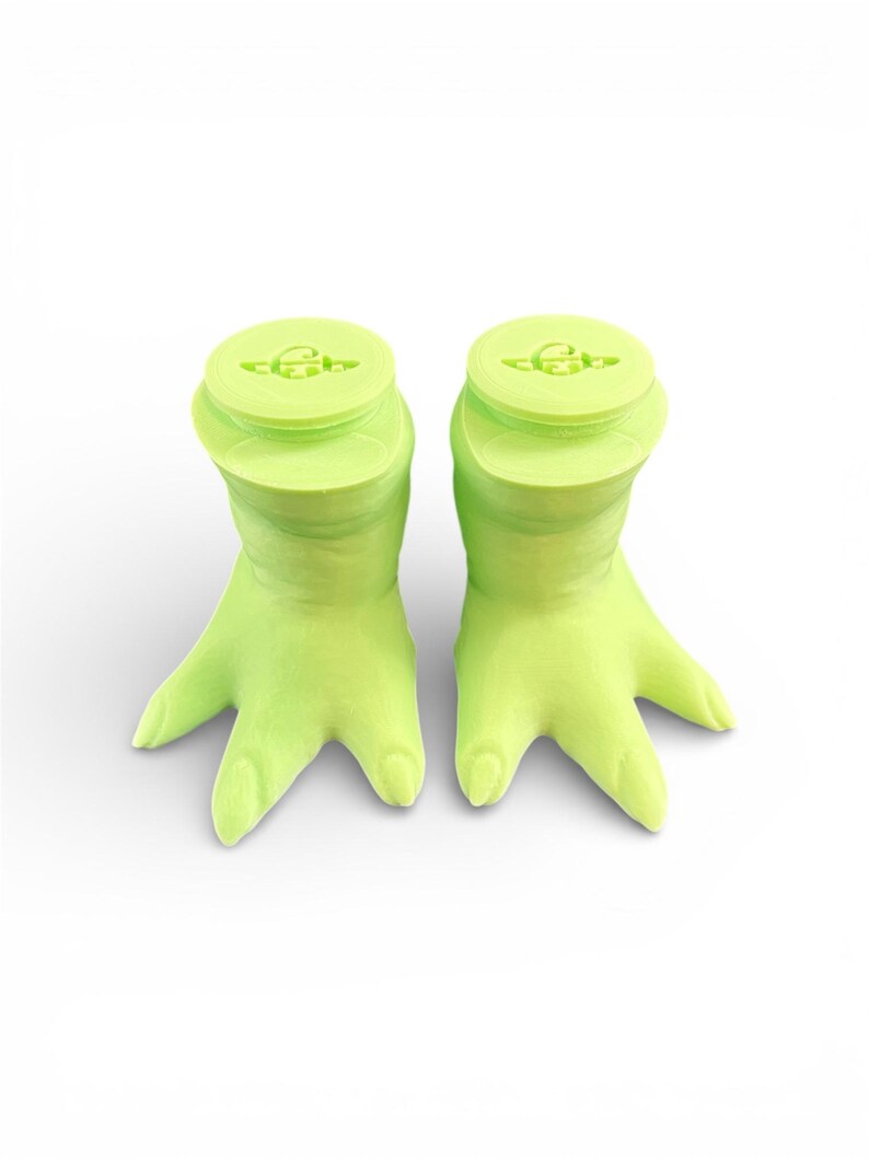 May include: Two lime green hand-shaped bottle stoppers. Each stopper has a round top with a small design and a hand-shaped base with three fingers. The stoppers are made of a solid, smooth material and are set against a white background.