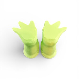 May include: Two lime green, foot-shaped ear plugs. The ear plugs are made of a soft material and have a three-pronged design. The ear plugs are designed to fit comfortably in the ear canal.