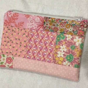May include: A pink patchwork zippered pouch with a variety of floral patterns. The pouch is made of cotton fabric and has a white zipper.