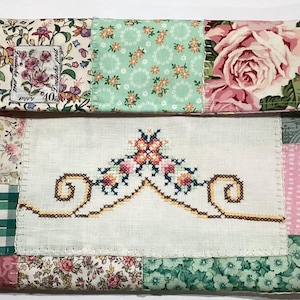 May include: A patchwork clutch bag with floral and geometric patterns in pink, green, and white. The design includes a central embroidered panel with a floral motif and a vintage postage stamp.