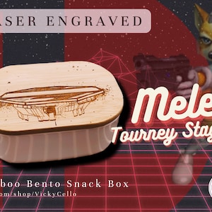 May include: A laser engraved wooden box with a drawing of a video game stage on the lid. The box is labeled "Bamboo Bento Snack Box" and has the text "etsy.com/shop/VickyCello" below. The background is a red and black grid with the text "Melee Tourney Stages" and a cartoon fox holding a gun.