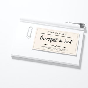 Breakfast in bed coupon card on white notebook paper with paperclip and white pen on desk