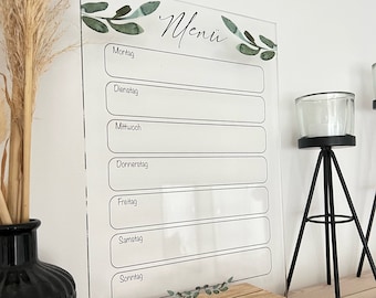 Może przedstawiać: Przezroczysta akrylowa tablica menu tygodniowego z drewnianą podstawą. Tablica ma zielony wzór liści, a dni tygodnia są wymienione po niemiecku: Montag, Dienstag, Mittwoch, Donnerstag, Freitag, Samstag, Sonntag.
