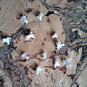 May include: A collection of small, white, abstract-shaped objects scattered on a textured, brown surface with dark, swirling patterns. The objects appear to be made of a smooth material and are evenly spaced.