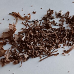 May include: A collection of dried, brown mushroom stems and caps, with a variety of shapes and sizes. Some pieces are light tan, while others are a darker brown. The image is a close-up, showing the texture and detail of the dried mushrooms.