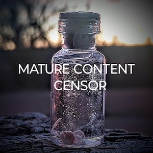 May include: A clear glass bottle with a dark stopper, containing a small, light-colored object. The bottle is labeled with the text "MATURE CONTENT CENSOR" in white. The background features a blurred, dusky landscape.