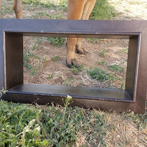 May include: A rectangular, dark brown wooden shelf with a distressed finish. The shelf is open on both sides and sits on grass. The shelf is a decorative item.